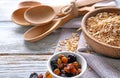 Bowl with raw oatmeal, raisins and spoons on wooden background