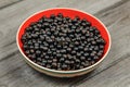 Bowl with red inside, full of blackcurrant, on wooden desk