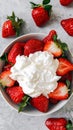 A bowl of ripe, juicy strawberries topped with a dollop of whipped cream, ready to be enjoyed on a textured surface. Royalty Free Stock Photo