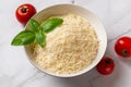 Bowl of shredded parmesan over marble background. Grated grana padano cheese and red tomatoes prepared for cooking. Delicious