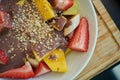 Bowl of sliced fruits and berries with chocolate souse and crushed walnuts standing on a wood board