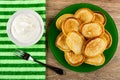 Bowl with sour cream, fork on napkin, fried pancakes in plate on wooden table. Top view