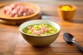 bowl of split pea soup with ham garnish on wooden table