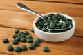 Bowl and spoon with spirulina tablets on wooden table Royalty Free Stock Photo