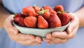 A bowl of strawberries held in two hands by a girl in pastel blue clothes Royalty Free Stock Photo