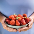 A bowl of strawberries held in two hands by a girl in pastel blue clothes Royalty Free Stock Photo