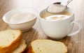 Bowl with sugar, slices of bread, spoon with sugar above white cup with fermented baked milk on wooden table Royalty Free Stock Photo