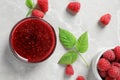 Bowl of sweet jam with ripe raspberries and green leaves on white table Royalty Free Stock Photo