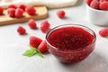 Bowl of sweet jam with ripe raspberries on white table, closeup. Royalty Free Stock Photo