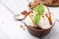 Bowl of tasty ice cream with caramel sauce, mint and nuts on white wooden table, closeup. Space for text Royalty Free Stock Photo