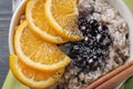 Bowl with tasty oatmeal, berries, sliced orange and poppy seeds, closeup