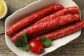 Bowl with thin dry smoked sausages, tomato and parsley on old wooden table, flat lay Royalty Free Stock Photo