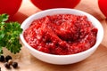 Bowl of tomato paste close-up with parsley, tomatoes and black pepper on wooden background