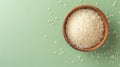 Bowl of uncooked white rice on a textured light green background. Top view. Concept of culinary staple, raw rice