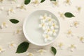 Bowl with water and beautiful jasmine flowers on white wooden table, flat lay Royalty Free Stock Photo