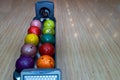 Bowling balls lie in a holder in a line. Colored balls and bowling