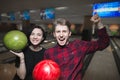 Bowling game. Happy young people with bowling balls lifted their hands upward with joy. Bowling players have won Royalty Free Stock Photo