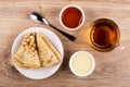 Bowls with apricot jam, condensed milk, pancakes on saucer, tea, spoon on table. Top view Royalty Free Stock Photo