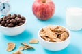 Bowls with cereal and chocolate balls, a glass of milk, an apple and an alarm clock on a blue background. Scheduled breakfast. Royalty Free Stock Photo