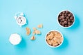 Bowls with cereal flakes and chocolate balls, a glass of milk and an alarm clock on a blue background. Scheduled breakfast, choice Royalty Free Stock Photo