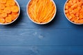 Bowls with cut fresh juicy carrots on blue wooden table, flat lay. Space for text Royalty Free Stock Photo