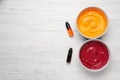 Bowls of different cream with food coloring and bottles of bright liquid on white wooden table, flat lay. Space for text Royalty Free Stock Photo