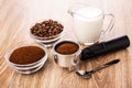 Bowls with ground coffee and coffee beans, holder from coffee maker with coffee, jug of milk, spoon on table Royalty Free Stock Photo