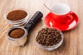 Bowls with ground coffee and coffee beans, holder from coffee maker with coffee, spoon in cup on saucer on table Royalty Free Stock Photo