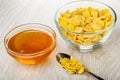 Bowls with honey and corn flakes, spoon with cornflakes on wooden table Royalty Free Stock Photo