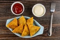 Bowls with ketchup and mayonnaise, fried pies samsa in plate, fork on wooden table. Top view