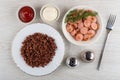 Bowls with ketchup, mayonnaise, plate with red boiled rice, bowl with fried pieces of sausages, salt, pepper, fork on table. Top Royalty Free Stock Photo