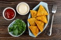 Bowls with ketchup and mayonnaise, parsley in bowl, fried pies samsa in plate, fork on wooden table. Top view Royalty Free Stock Photo