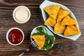 Bowls with ketchup and mayonnaise, samsa on fork above bowl with parsley, fried pies samsa in oval plate on wooden table. Top Royalty Free Stock Photo