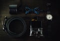 Bowtie, perfume bottle, leather belt, ring box and silver wristwatch on the table.