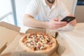 A box of appetizing pizza is on the table. A man uses a phone on the background of an open box of tasty pizza. Royalty Free Stock Photo