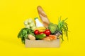 Box with different food ingredients such as fruits, vegetables, milk, yogurt, eggs on yellow background