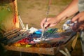 Box easel with canvas, oil paint, palette, and tools and Hand of painter with brush on nature outdoors Royalty Free Stock Photo