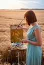 Back View Of Girl Painter With Red Hair, Drawing Wheat Field In Late Summer During Sunset