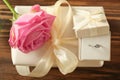 Box with engagement ring, rose and gift on wooden table