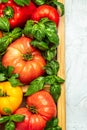 box of fresh, organically homegrown vegetables tomatoes, peppers and basil on a light background. vertical image. top view. place