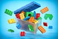 Box full of colorful toy plastic bricks and blocks on blue background. Delivery children gifts and toys