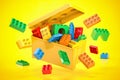 Box full of colorful toy plastic bricks and blocks on yellow background. Delivery children gifts and toys
