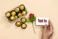 Box of golden premium chocolate sweets with closeup hand holding a thank you card, rose flower for valentine`s holiday