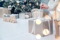 Box with Luxury Metallics gift on background of Christmas tree. Hands open New Year`s gift close-up, copy space