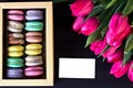 Box with macaroons and a bouquet of tulips and a card for your text on a dark background.