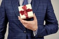 Box pack tied with elegant red ribbon being held in male hand formal style for holiday celebration, gift