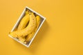 Box of ripe bananas on vivid yellow background