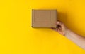 Box for shipment is held by female hand.nDetail of delivery cardboard box with label, isolated on yellow background.