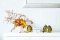 Box with text HELLO AUTUMN, decorative striped pumpkins and vase with bouquet of falling leaves and fern on a white chest, table