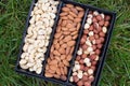 Box with three kinds of nuts, cashews, hazelnuts, almonds. Grass background. Top view